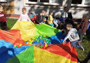dzieci zbierają kolorowe piłki i wrzucają na chustę